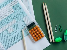 Flat lay of tax forms, calculator, pencils, and clips on green surface, ideal for finance or accounting themes.
