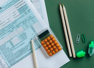 Flat lay of tax forms, calculator, pencils, and clips on green surface, ideal for finance or accounting themes.