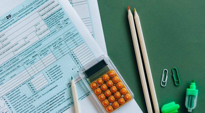 Flat lay of tax forms, calculator, pencils, and clips on green surface, ideal for finance or accounting themes.