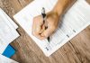 Jersey City Seniors to Get Help Applying for Property Tax Freeze Hand writing on a W-9 tax form using a ballpoint pen on wooden desk.