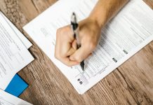 Hand writing on a W-9 tax form using a ballpoint pen on wooden desk.