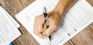 Hand writing on a W-9 tax form using a ballpoint pen on wooden desk.