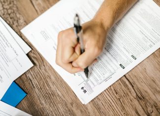 Hand writing on a W-9 tax form using a ballpoint pen on wooden desk.