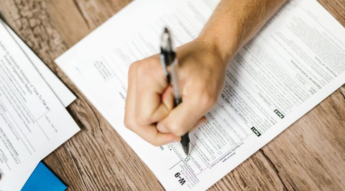 Jersey City Seniors to Get Help Applying for Property Tax Freeze Hand writing on a W-9 tax form using a ballpoint pen on wooden desk.