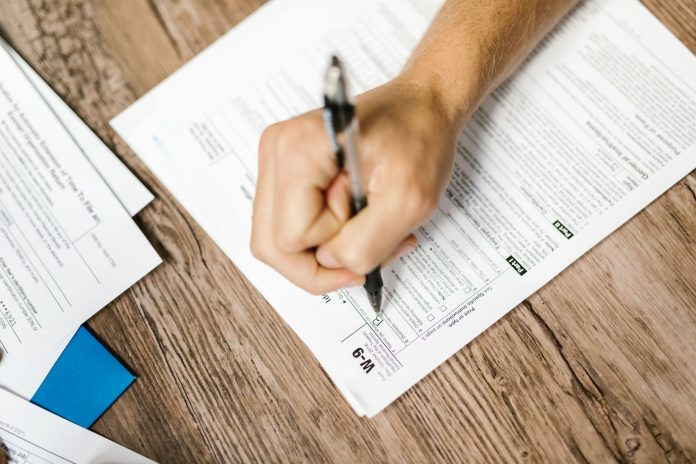 jersey-city-seniors-to-get-help-applying-for-prope Hand writing on a W-9 tax form using a ballpoint pen on wooden desk.