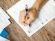 Jersey City Seniors to Get Help Applying for Property Tax Freeze Hand writing on a W-9 tax form using a ballpoint pen on wooden desk.