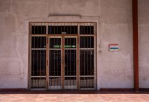 Judge lifts order blocking state oversight of Heights hospital closure A rustic iron gate in a textured wall with a warning sign, captured in bright daylight.