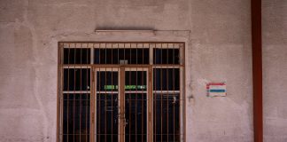 A rustic iron gate in a textured wall with a warning sign, captured in bright daylight.