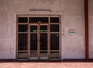 A rustic iron gate in a textured wall with a warning sign, captured in bright daylight.