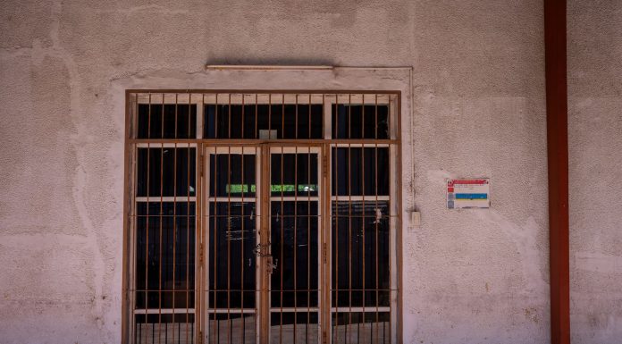 A rustic iron gate in a textured wall with a warning sign, captured in bright daylight.