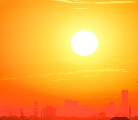A city skyline silhouetted against a vivid, orange sunset sky.