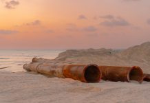 Rusty pipes at a coastal construction site with scenic sunset view.