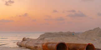 Rusty pipes at a coastal construction site with scenic sunset view.