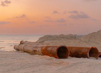 Rusty pipes at a coastal construction site with scenic sunset view.