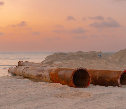 Rusty pipes at a coastal construction site with scenic sunset view.
