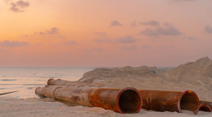 Rusty pipes at a coastal construction site with scenic sunset view.