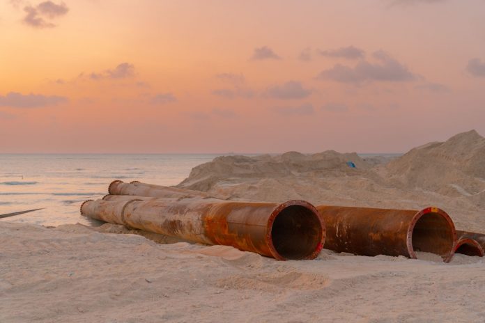 Rusty pipes at a coastal construction site with scenic sunset view.