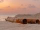 Rusty pipes at a coastal construction site with scenic sunset view.