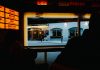 View from inside a dimly lit bar to a street outside with cafe and pedestrians.