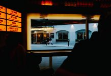 View from inside a dimly lit bar to a street outside with cafe and pedestrians.
