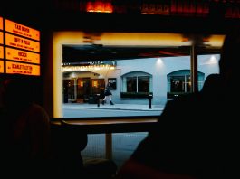 View from inside a dimly lit bar to a street outside with cafe and pedestrians.