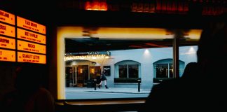 View from inside a dimly lit bar to a street outside with cafe and pedestrians.