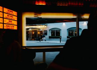 View from inside a dimly lit bar to a street outside with cafe and pedestrians.