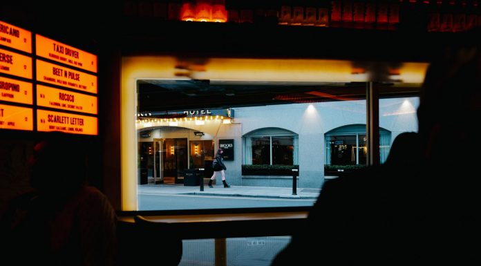 View from inside a dimly lit bar to a street outside with cafe and pedestrians.