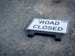 A road closed sign lies on a gravel pathway, indicating a blocked road ahead.