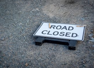 A road closed sign lies on a gravel pathway, indicating a blocked road ahead.