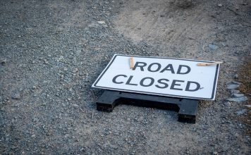 A road closed sign lies on a gravel pathway, indicating a blocked road ahead.