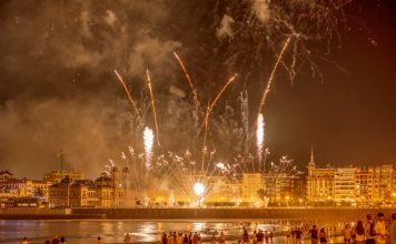 Vibrant fireworks light up the night sky over a bustling waterfront city, captivating an excited crowd below.