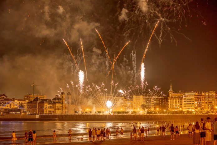 Vibrant fireworks light up the night sky over a bustling waterfront city, captivating an excited crowd below.