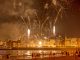 Vibrant fireworks light up the night sky over a bustling waterfront city, captivating an excited crowd below.
