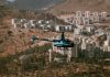 Aerial view of a helicopter flying over a town surrounded by hills and trees