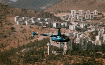 Aerial view of a helicopter flying over a town surrounded by hills and trees