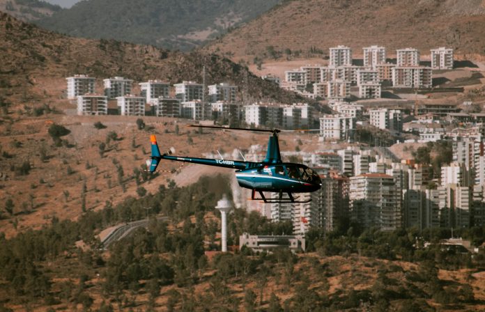 Aerial view of a helicopter flying over a town surrounded by hills and trees