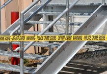 Close-up of a metal stairway blocked by yellow police crime scene tape outdoors.