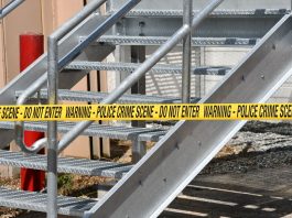 Close-up of a metal stairway blocked by yellow police crime scene tape outdoors.