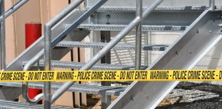 Close-up of a metal stairway blocked by yellow police crime scene tape outdoors.
