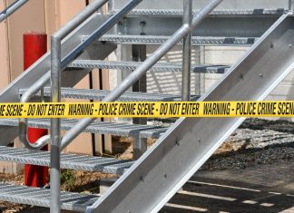 Close-up of a metal stairway blocked by yellow police crime scene tape outdoors.