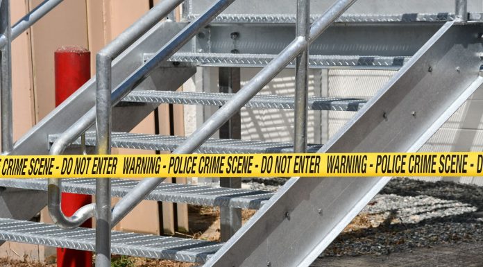 Close-up of a metal stairway blocked by yellow police crime scene tape outdoors.