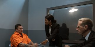 A tense interrogation scene with lawyers questioning an inmate in a prison setting.