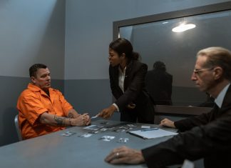 A tense interrogation scene with lawyers questioning an inmate in a prison setting.