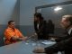 A tense interrogation scene with lawyers questioning an inmate in a prison setting.