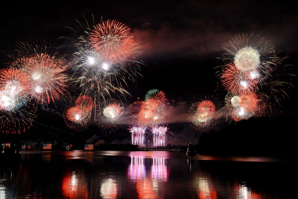 Vibrant fireworks illuminate the night sky, reflecting brilliantly over the calm lake surface.