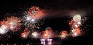 Vibrant fireworks illuminate the night sky, reflecting brilliantly over the calm lake surface.