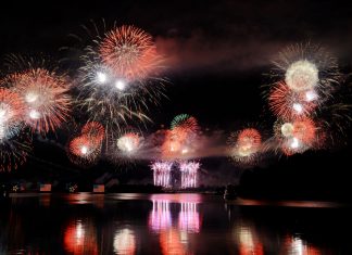 ÚLTIMA HORA: Fiesta del 4 de Julio regresa a Hoboken en 2026 Vibrant fireworks illuminate the night sky, reflecting brilliantly over the calm lake surface.