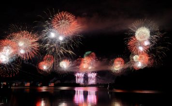 Vibrant fireworks illuminate the night sky, reflecting brilliantly over the calm lake surface.