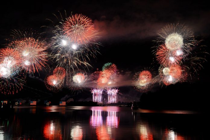 Vibrant fireworks illuminate the night sky, reflecting brilliantly over the calm lake surface.